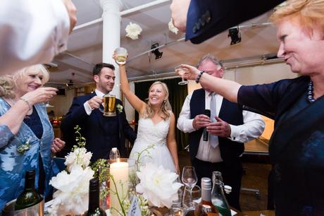 Bride, groom & gusts raise glasses of beer and champagne for a toast. 