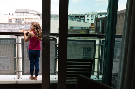 Little flower girl stands on balcony at London wedding. 