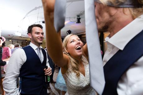 Bride puts tie on guest's head during fun wedding party. 