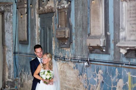 Bride & groom next to crumbling pale blue wall in de-consecrated church at The Asylum in London. 