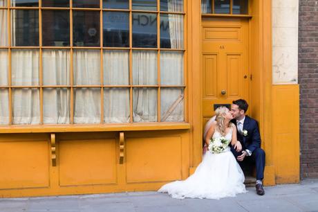 Bride & Groom kissing in doorway in front of yellow London building. 