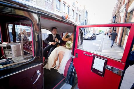 Fun bride necks prosecco in vintage car at London wedding. 