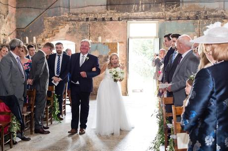 Bride makes happy face as she walks up aisle at Asylum wedding venue. 