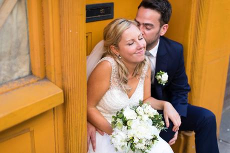 Groom kisses cute bride on the cheek at London wedding near yellow walls. 