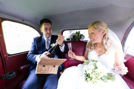 Bride and groom open champagne in car. 