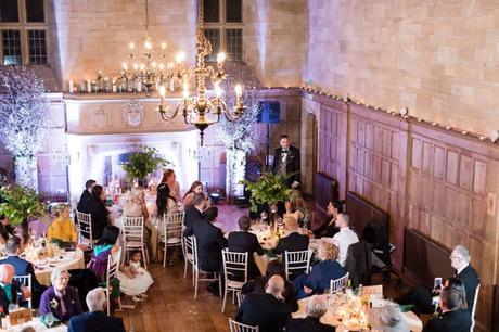 Wide shot of groom giving his speech in a wood- panelled room. 
