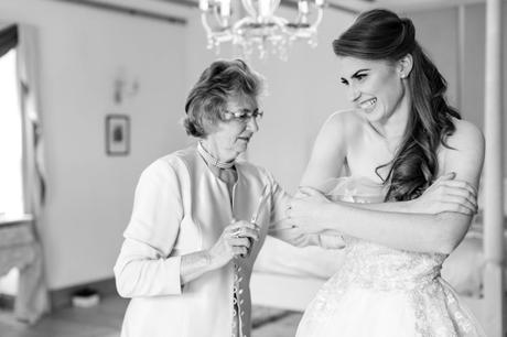 Bride's grandmother helps her into her dress in black and white wedding photograph