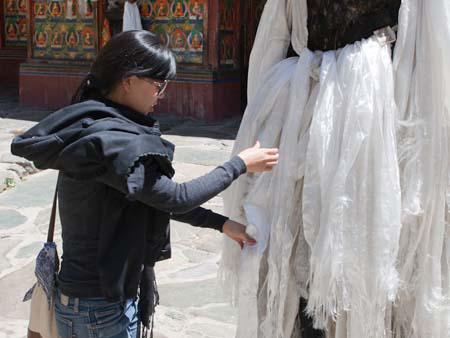 Sonya tying a white scarf to the prayer pole in the courtyard
