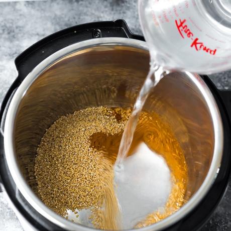 pouring water into an instant pot containing steel cut oats and cinnamon