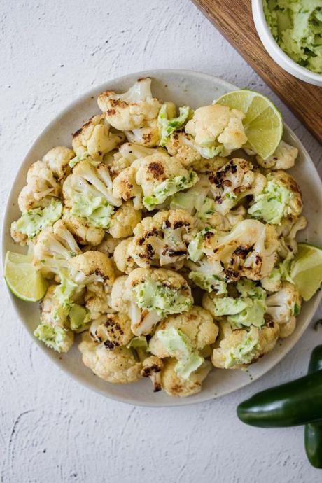 overhead view of a bowl of grilled cauliflower with jalapeno lime butter dolloped all over