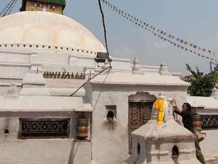 Sonya tying a white scarf to a smaller stupa in front of the Bodhnath Stupa