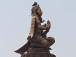 The man-bird Garuda kneels with folded arms on top of a column facing the Krishna Mandir Temple