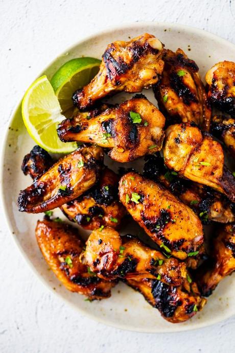 overhead view of thai grilled chicken wings on plate with lime wedges