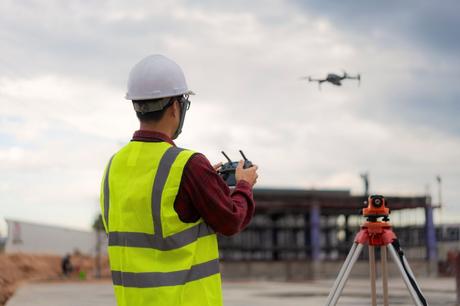 Asian construction worker piloting drone at building site. 