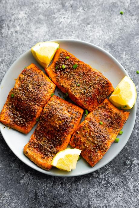 overhead view of plate with four air fryer salmon portions and lemon wedges