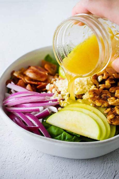 pouring vinaigrette over apple bacon spinach salad