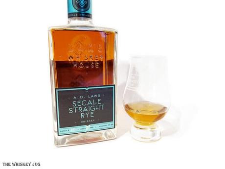 White background tasting shot with the A.D. Laws Secale Rye Whiskey bottle and a glass of whiskey next to it.
