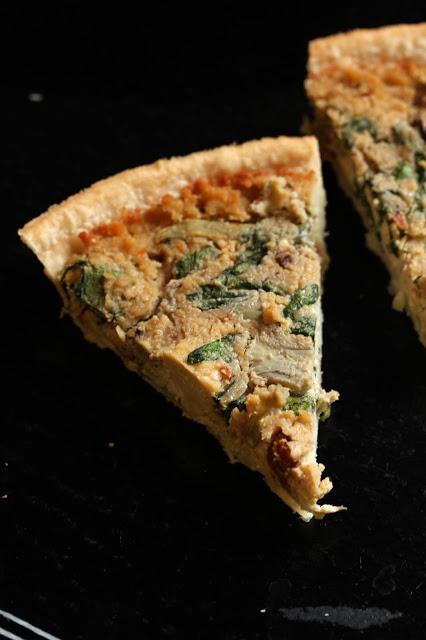 a slice of quiche with sundried tomato pieces, spinach, artichokes, and mushroom slices.