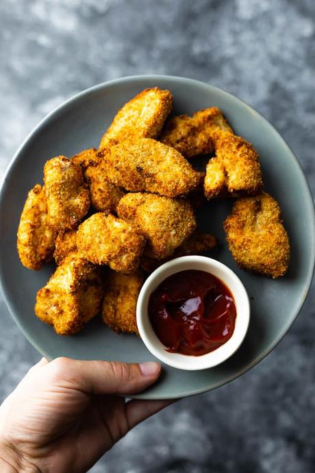 hand holding a plate of air fryer chicken nuggets