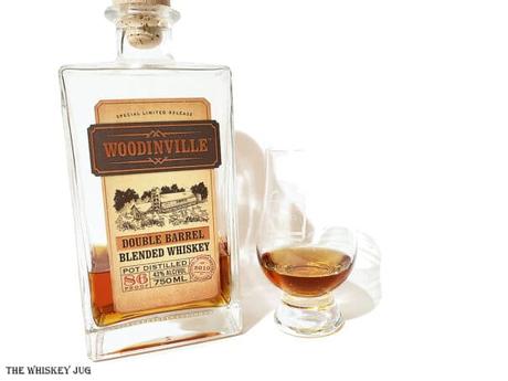 White background tasting shot with the Woodinville Double Barrel Blended Whiskey bottle and a glass of whiskey next to it.