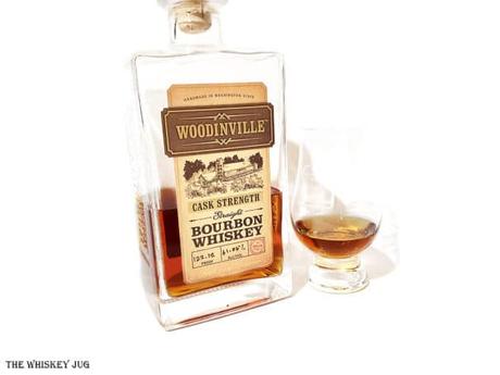 White background tasting shot with the Woodinville Cask Strength Bourbon Whiskey bottle and a glass of whiskey next to it.
