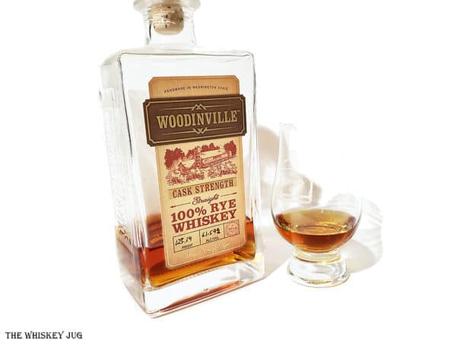 White background tasting shot with the Woodinville Cask Strength Rye Whiskey bottle and a glass of whiskey next to it.