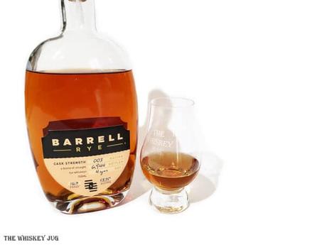 White background tasting shot with the Barrell Rye Batch 003 bottle and a glass of whiskey next to it.