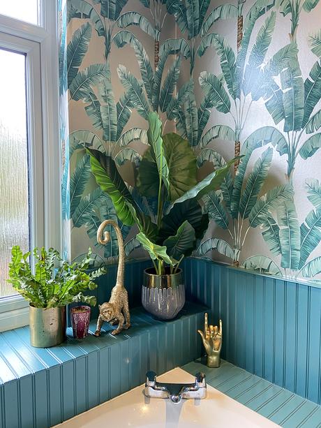 Tropical patterned wallpaper with artificial house plants and gold monkeys to give a jungle feel