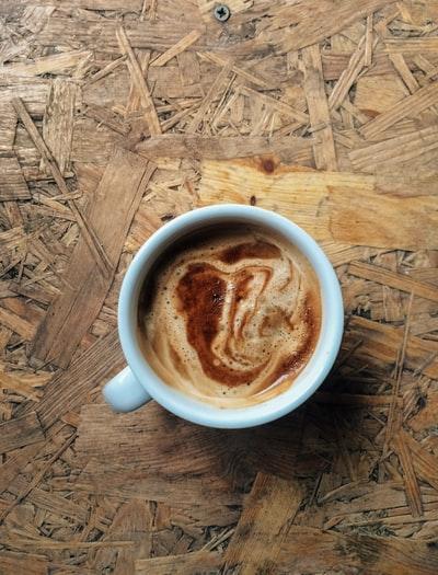 A vertical high angle closeup shot of espresso coffee in a white ceramic coffee cup on wooden surface