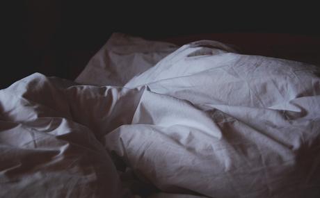 Muted photo of a bed with rumpled bedsheets.