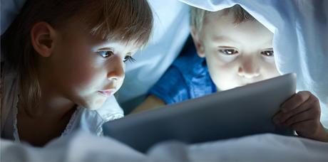 cute little children lying under blanket with tablet computer