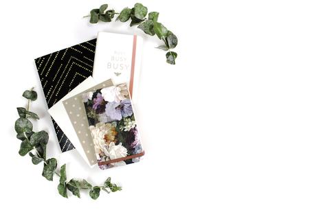 Flatlay photograph featuring pile of notebooks and leaves surrounding.