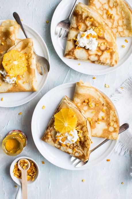 a few plates of crepes with oranges and honey as the toppings