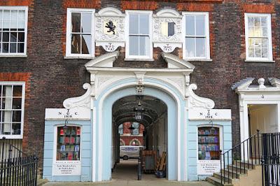 The ground and first floors of part of a Georgian brick building with sash windows. In the center is an alley passing through the building, with a stucco frontage including a split pediment and scrolls painted white, and a light blue-painted frontage with two windows displaying law books.