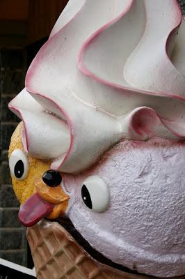 Photo showing part of a large fibre-glass ice cream cone with swirls of soft-serve ice cream and a disturbing face with the tongue poking out.