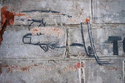 A small section of a red brick wall, painted grey-white wiht a painted outline of a pointing hand, incuding fingernail and cuff details.