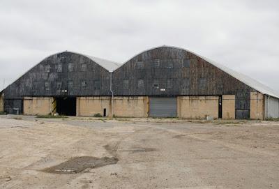 Exterior photograph of the warehouse. The view of the buildling is similar to that in the photograph above, but there is no road leading up to the building: instead, the foreground shows bare earth.