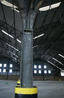 Photograph of the interior with steel pillars and struts and a corrugated iron roof. The interior is otherwise empty; the front gable wall and windows are visible in the distance.