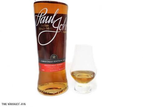 White background tasting shot with the Paul John Christmas Edition 2020 bottle and a glass of whiskey next to it.