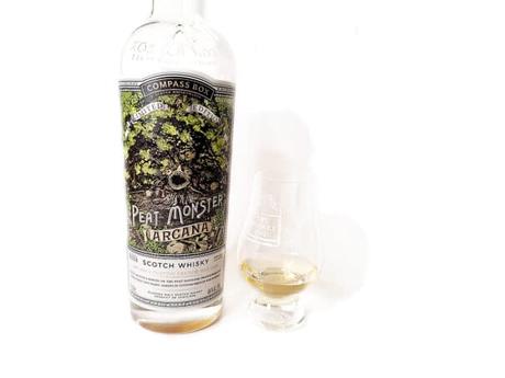 White background tasting shot with the Peat Monster Arcana bottle and a glass of whiskey next to it.