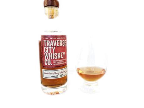 White background tasting shot with the Traverse City American Cherry Whiskey bottle and a glass of whiskey next to it.