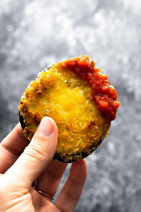 hand holding air fried eggplant dipped in marinara sauce