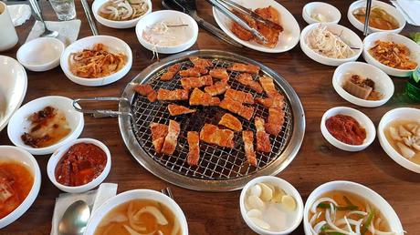 grilled meat in the middle surrounded by many korean dishes