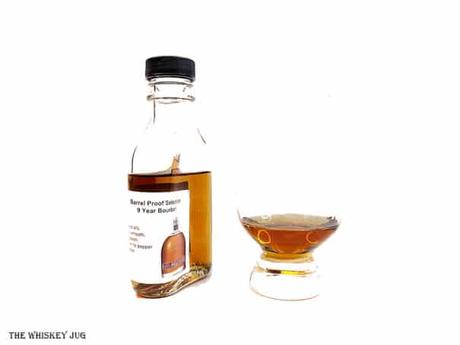 White background tasting shot with the Redemption 9 Year Barrel Proof Bourbon bottle and a glass of whiskey next to it.