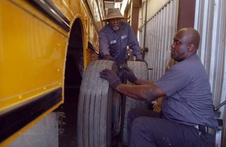 Frank Mann, standing, rolls a new tire toward Mike Ellison to mount onto one of the Jackson-Madison County school buses in preparation for the 2012-13 academic year.