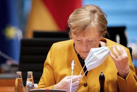 German Chancellor Angela Merkel takes down her face mask as she arrives for the weekly cabinet meeting of the German government at the chancellery in Berlin, Wednesday, March 24, 2021. In the background left Finance Minister and Vice Chancellor Olaf Scholz. (Kay Nietfeld/Pool via AP)