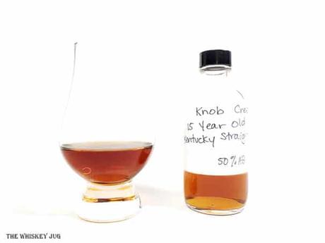 White background tasting shot with the Knob Creek 15 Years bottle and a glass of whiskey next to it.