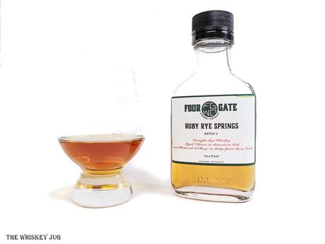 White background tasting shot with the  Four Gate Ruby Rye Springs bottle and a glass of whiskey next to it.