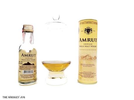 White background tasting shot with the Amrut Classic Indian Single Malt bottle and a glass of whiskey next to it.