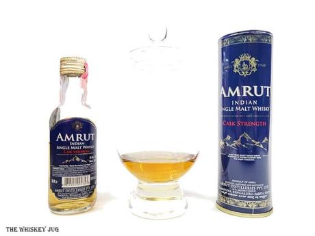 White background tasting shot with the Amrut Cask Strength Indian Single Malt bottle and a glass of whiskey next to it.